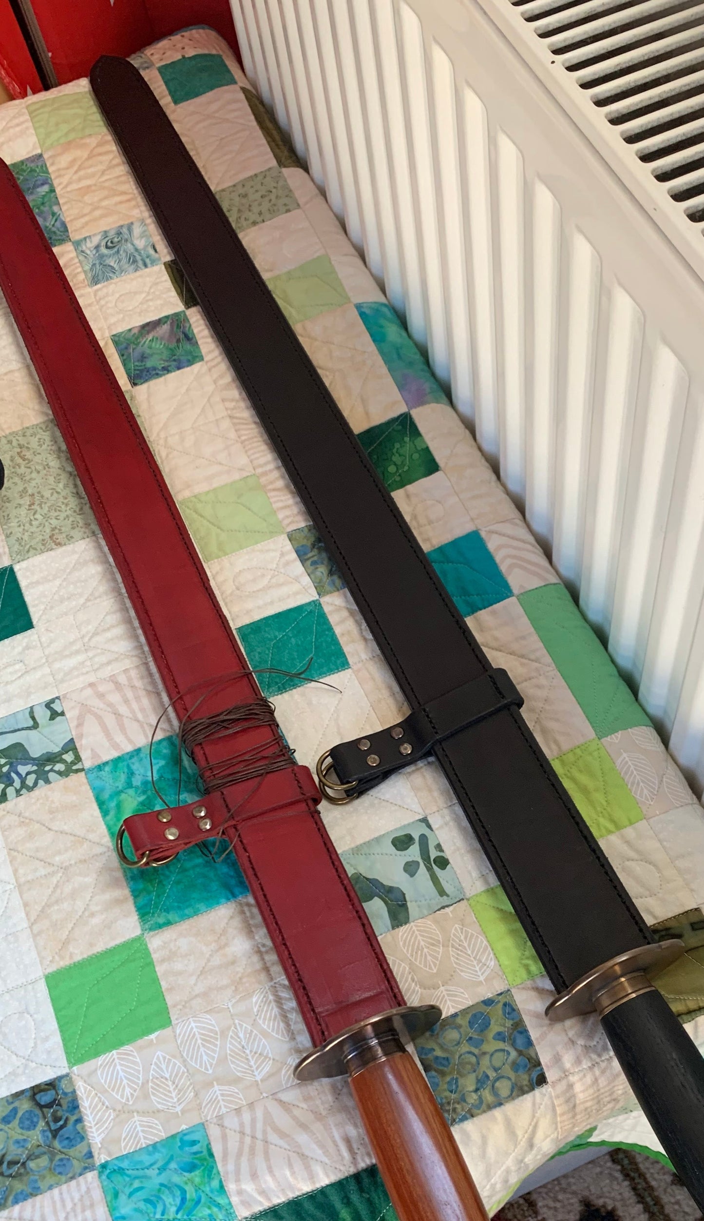 Two swords on a patterned quilt with a radiator in the background